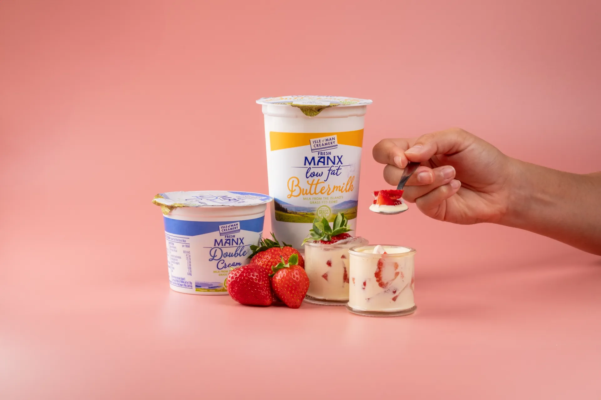 Product photography shot by DotPerformance for the Isle of Man Creamery Doorstep Delivery campaign, showing Fresh Manx Low Fat Buttermilk and Manx Double Cream with strawberries and cream desserts on a pink background